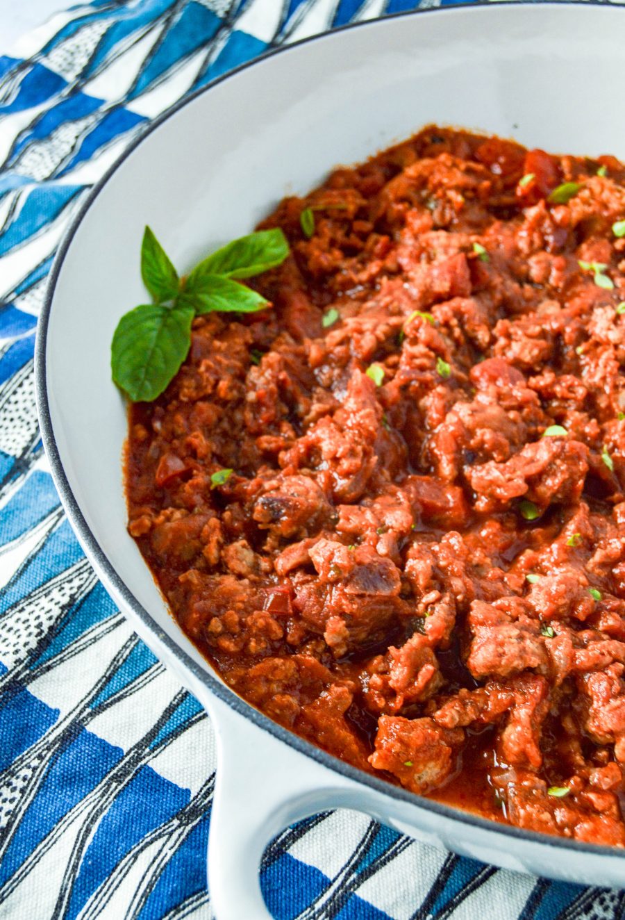angled close up of Spicy Sausage Marinara in white dish with blue, white and black towel behind it. www.atwistedplate.com/spicy-sausage-marinara/