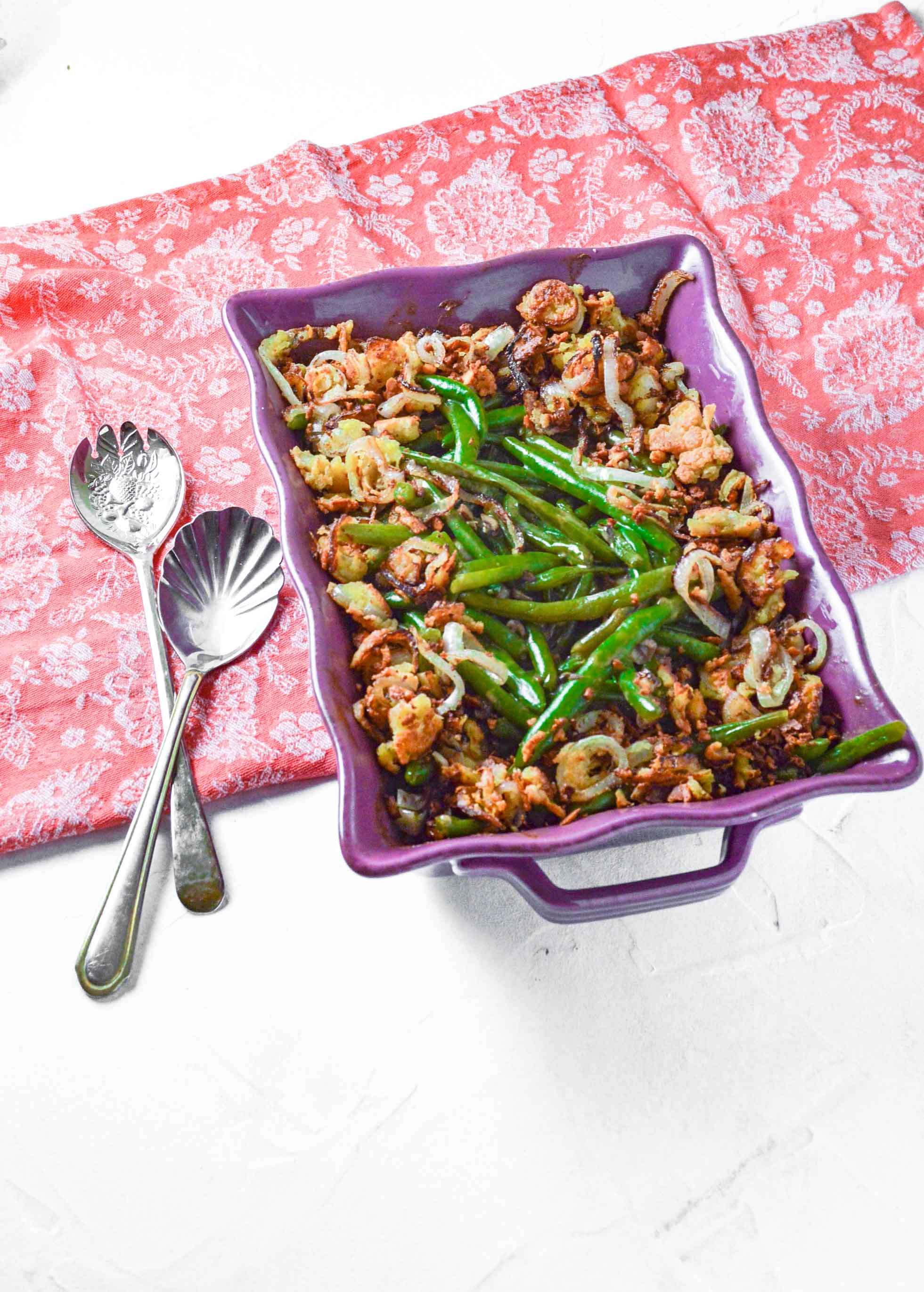 Angled view of Dairy Free Green Bean Casserole in a purple dish on a pink towel. https://www.atwistedplate.com/green-bean-casserole-gluten-dairy-free/