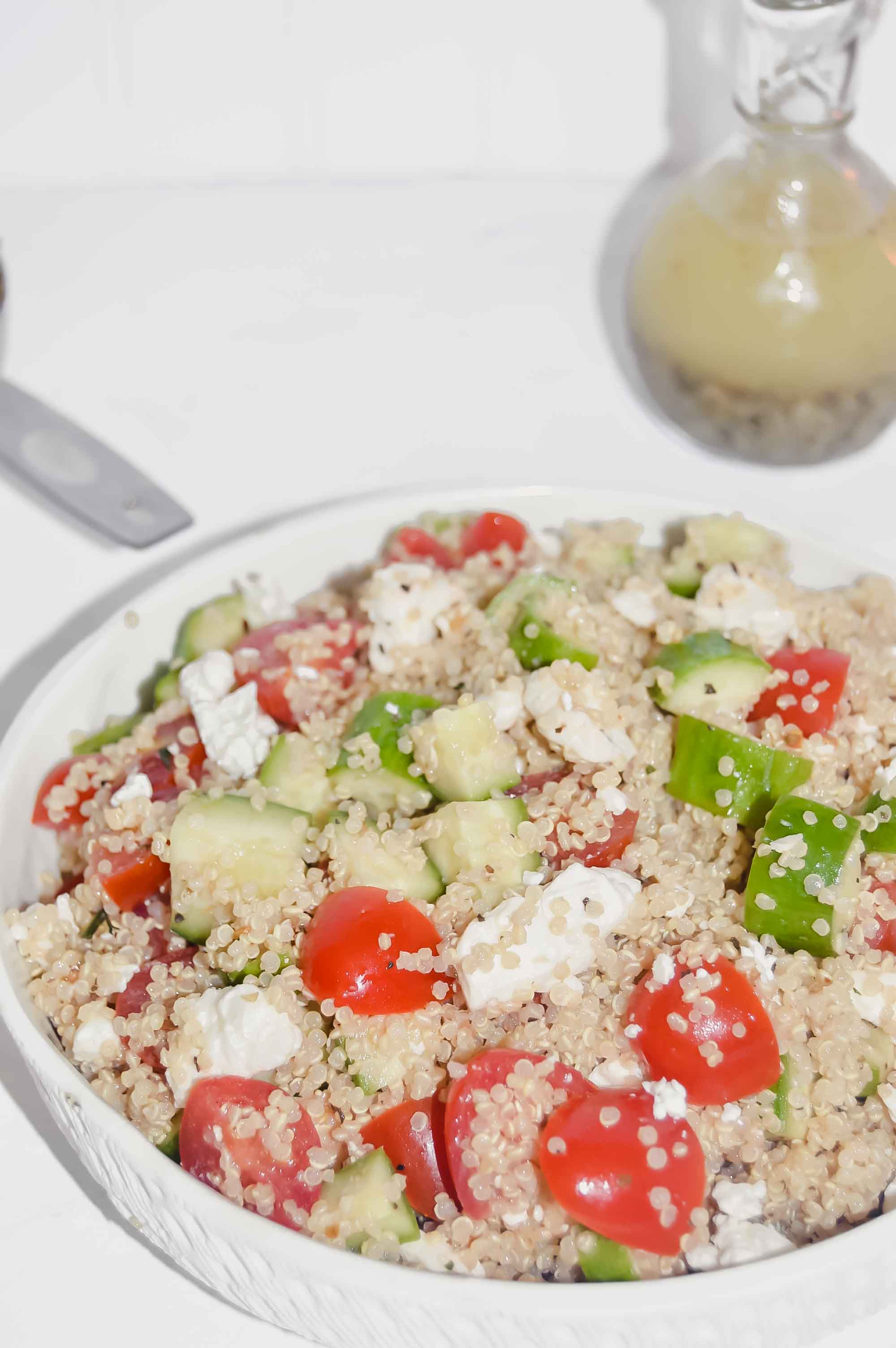 Quinoa Salad with Cucumber, Tomato and Feta with a bowl of tomatoes and a jar of Italian Seasoning behind it. www.atwistedplate.com