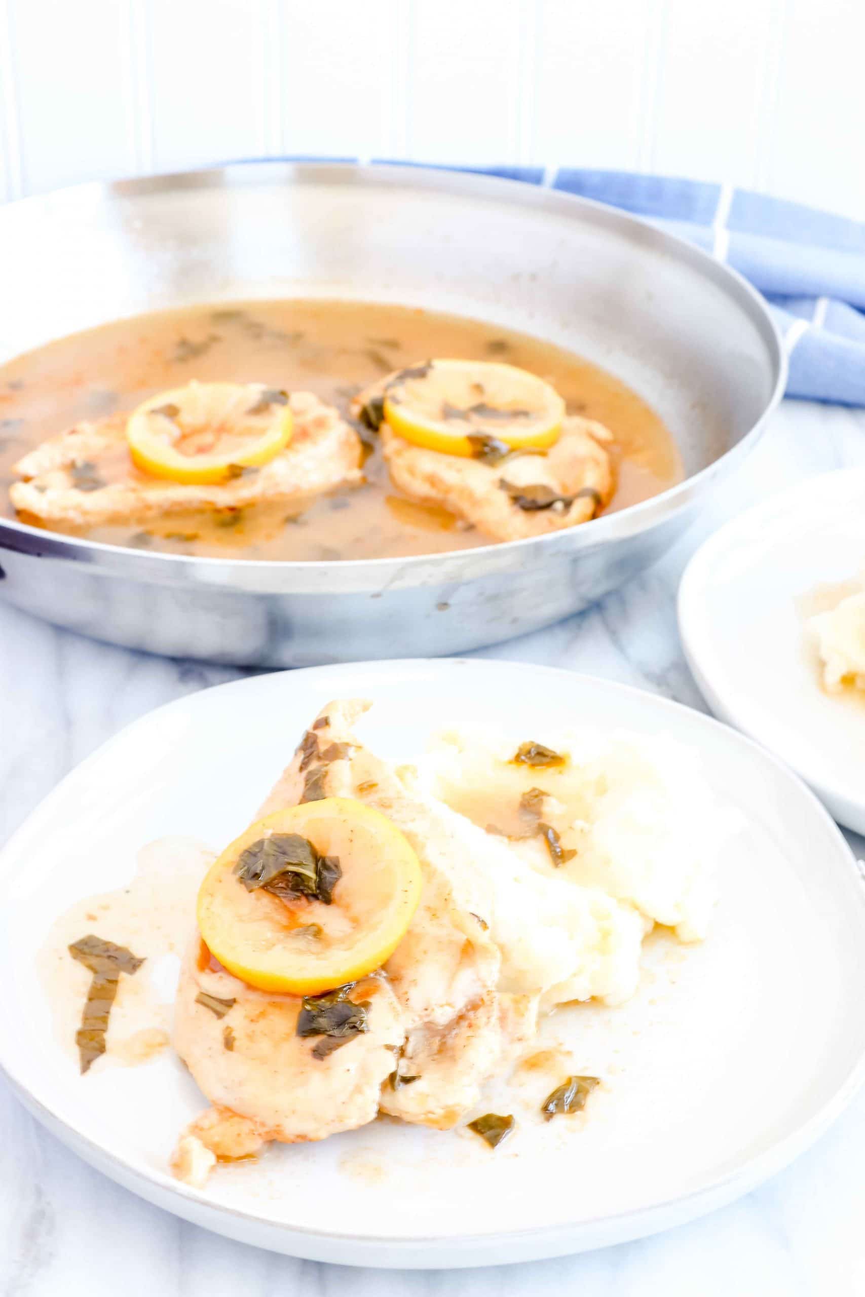 Angled view of Lemon Basil Chicken with 2 Chicken Breast in Sauté pan with the sauce. 2 white plates with Mashed Potatoes, the lemon basil chicken and sauce with 2 forks.
