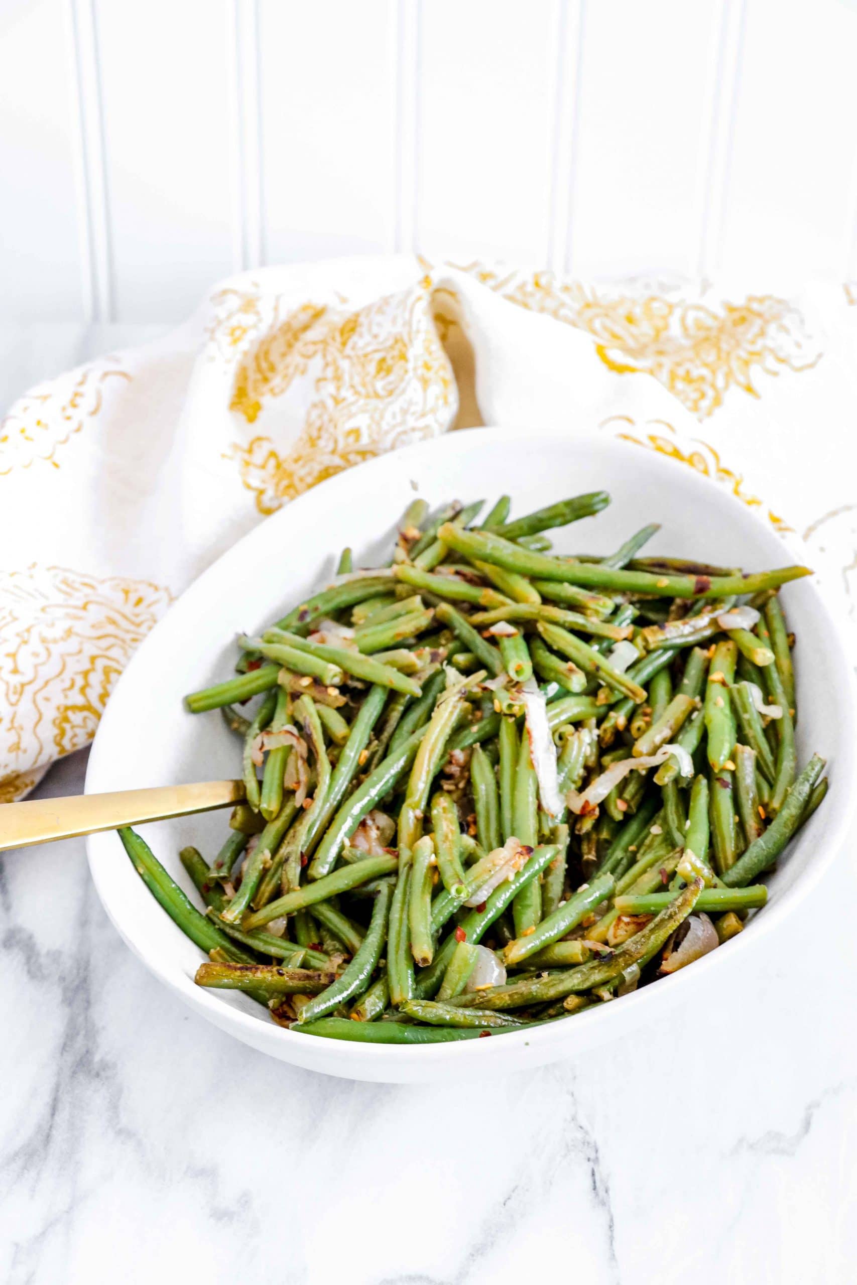 Over view of Spicy Green Beans on a round white bowl with a gold/white towel. www.atwistedplate.com/spicy-green-beans/
