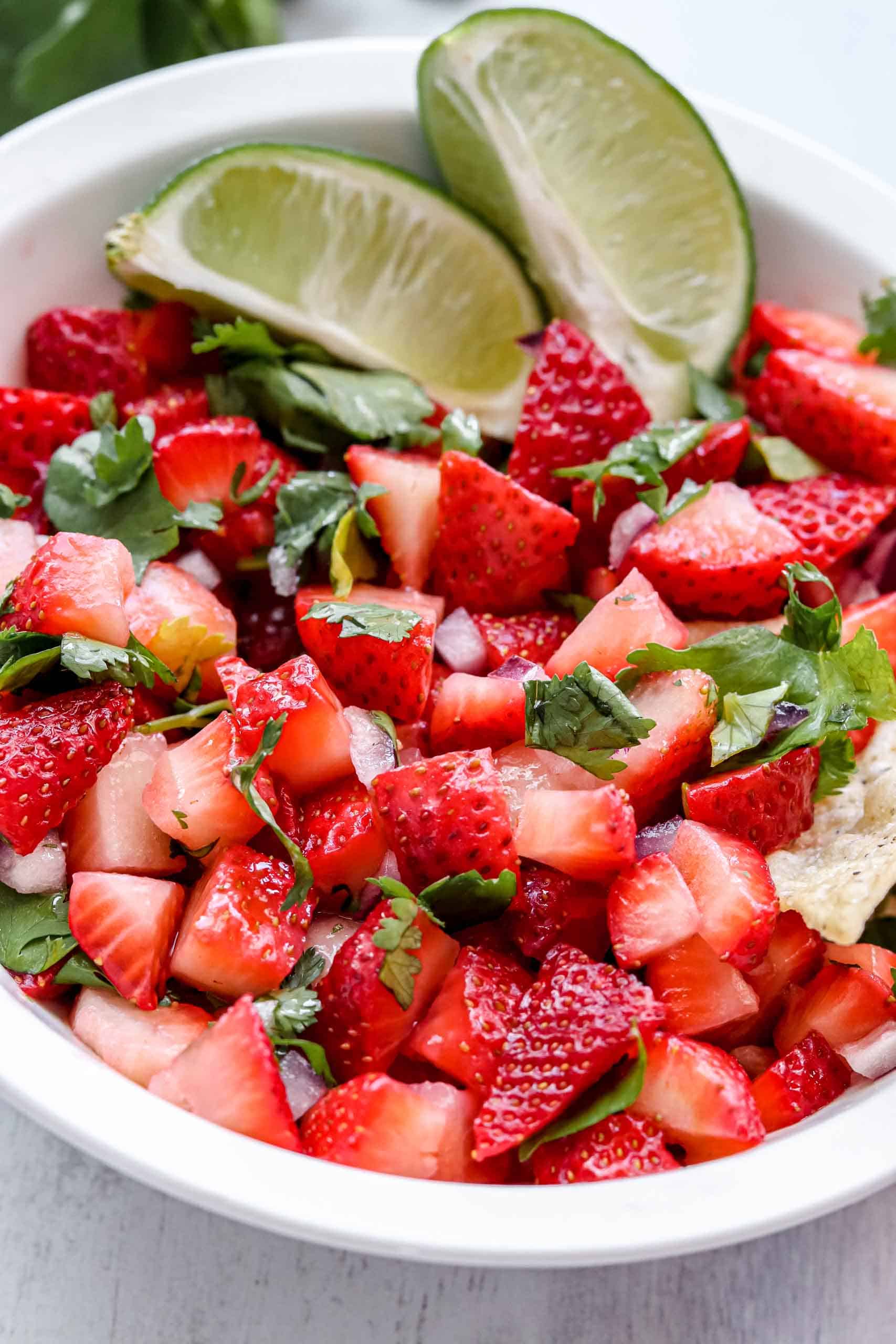 strawberry salsa image is a bowl of Strawberry salsa with 2 lime wedges. www.atwistedplate.com/strawberry-salsa/